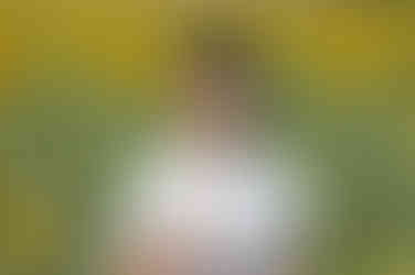 Băiat ținând o floare și zâmbind în mijlocul unui câmp de floarea-soarelui.