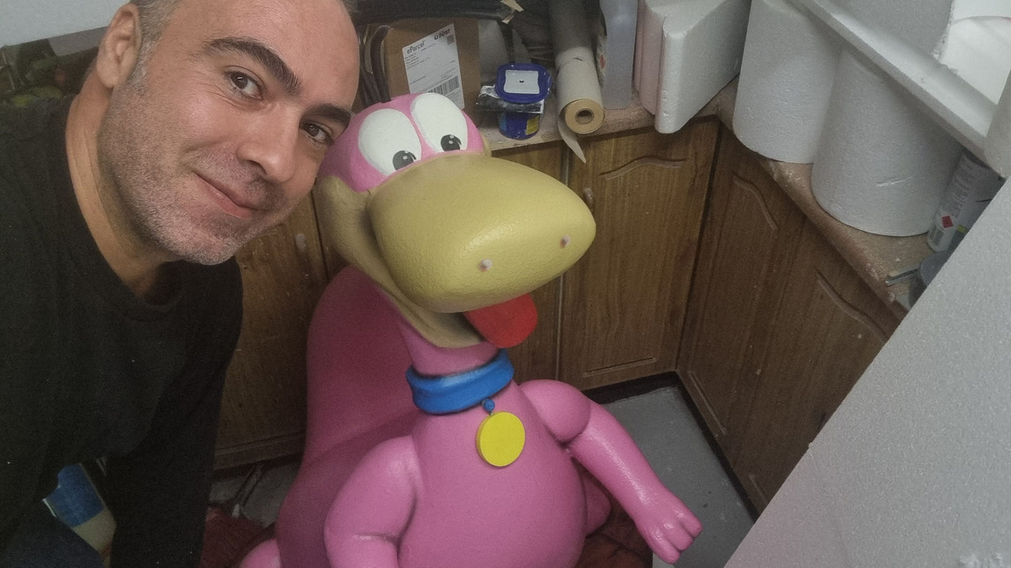Man with a pink dinosaur statue selfie, dinosaur wearing a blue collar.