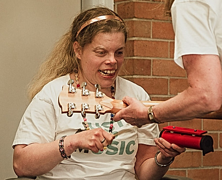 Picture of a woman holding a red chime bar and the arm of another woman playing guitar  to her