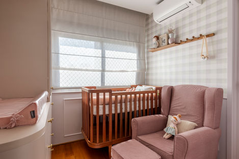 Quarto de criança em tons de rosa com berço em madeira, poltrona rosa e brinquedos