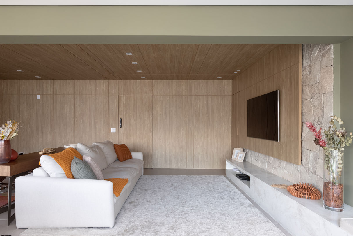 sala de tv revesida em madeira, tv, sofá branco e objetos em verde de laranja e verde