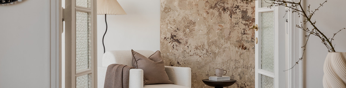 View through open doors onto a serene lounge with soft armchair, textured art, and calm, n
