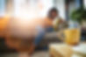Blur, coffee on table and cup for wellness with woman on sofa in living room of home to re