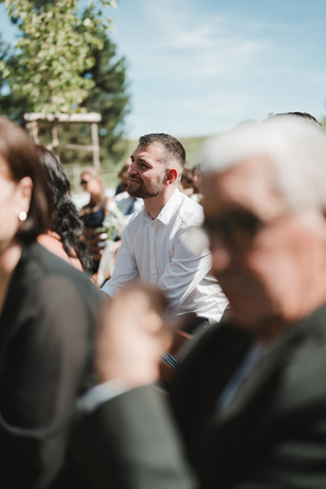 Gäste sitzen draußen in Reihen unter Sonnenschirmen und verfolgen die Trauung.