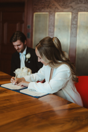 Braut beugt sich über den Tisch und setzt ihre Unterschrift auf die Heiratsurkunde.