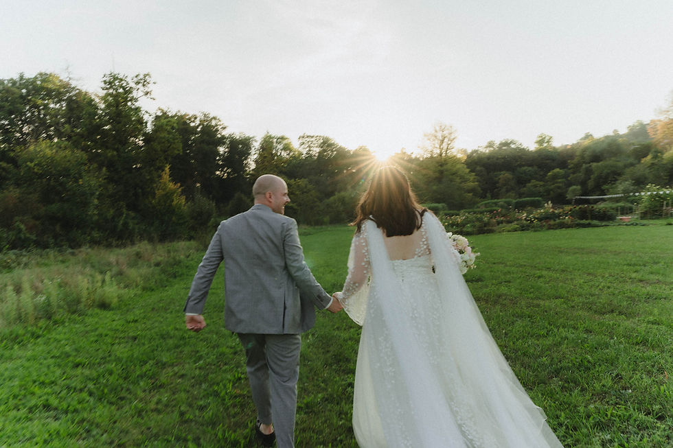Vor dem Licht des Sonnenuntergangs rennen Braut und Bräutigam lachend über eine Wiese.