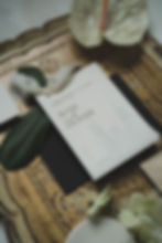 Hochzeitseinladung mit Text "Rose und Oliver" auf Tablett mit Pflanzen und Blüten, stilvoll arrangiert in natürlichen Farben.