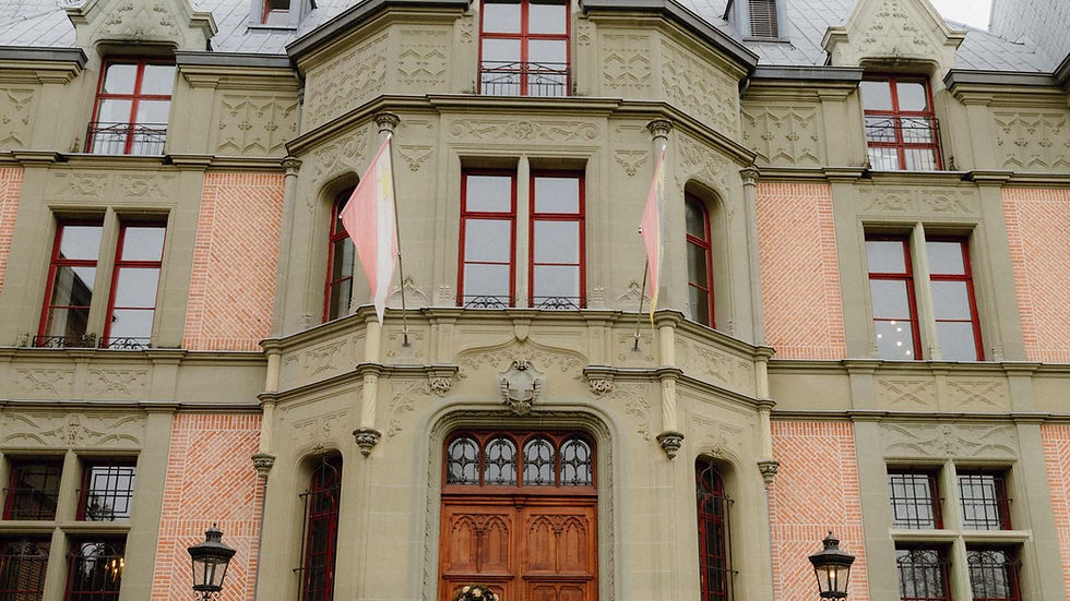 Historisches Gebäude mit roter Backsteinfassade, grünen Zierelementen und Holztüren, dekoriert mit Kranz. Schild mit Text "SCHADAU".