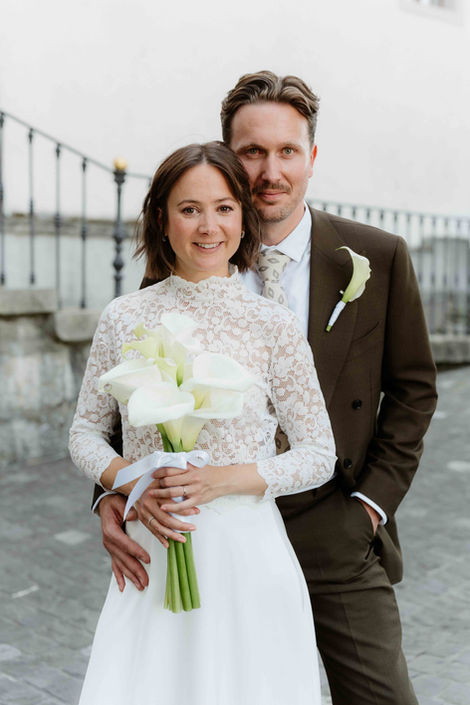 Brautpaar posiert am Seeufer, Braut in Spitzenkleid mit Bouquet.