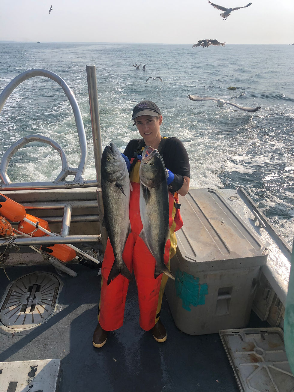 A white fisherwoman holds told large fish in each of her hands