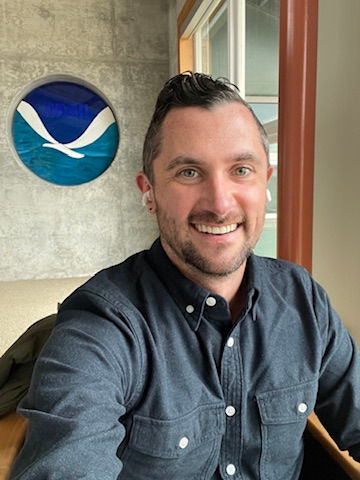 A white man poses next to the NOAA logo