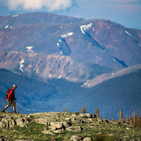 Man walking along a rocky ridge on top of a mountain with a large mountain range in background. Links to Leave No Trace in Breckenridge.
