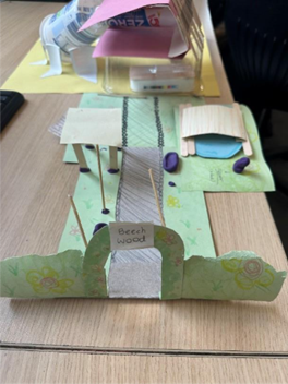 A model built from green card and various other bits of cardboard sits on the edge of a table.