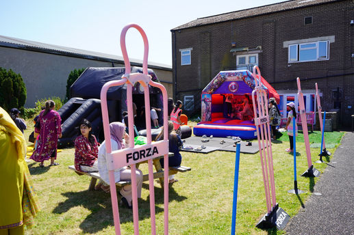 People gather at a sunny outdoor party with Marvel and black inflatable bounce houses, FORZA poles, and scattered shoes.