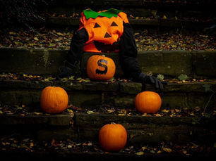 Pumpkin-headed scarecrow on stone steps with orange pumpkins. One pumpkin has an "S." Autumn leaves scattered on dark stones. Spooky mood.
