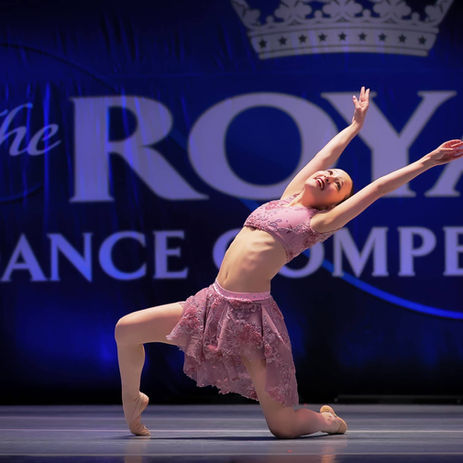 Solo dancer in pink costume performing contemporary back arch on stage at Royal Dance Competition