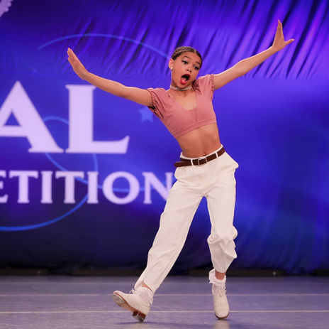 Solo dancer in white costume performing hip hop routine with arms raised at Royal Dance Competition