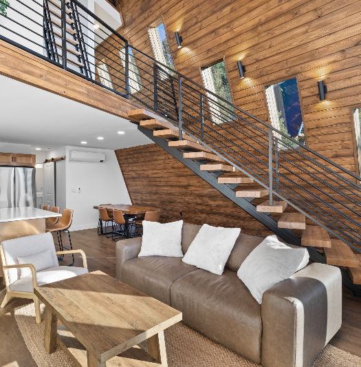 Living room interior of a luxury cabin near Zion National Park featuring a couch and staircase with wood accents and natural light in a Southern Utah vacation rental.