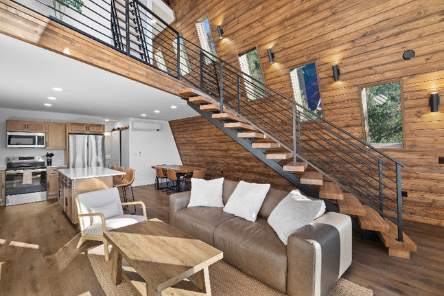 Living room interior of a luxury cabin near Zion National Park featuring a couch and staircase with wood accents and natural light in a Southern Utah vacation rental.