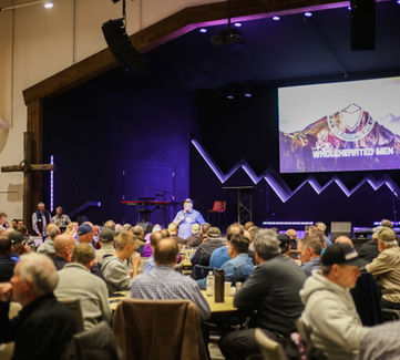 Men at a breakfast and livestream event in a church auditorium.