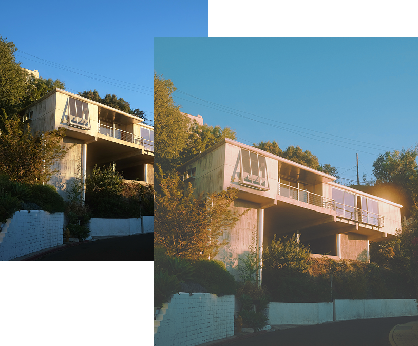 Modern house on stilts in a hilly area, surrounded by greenery. Clear sky with sunlight casting warm tones on the building.