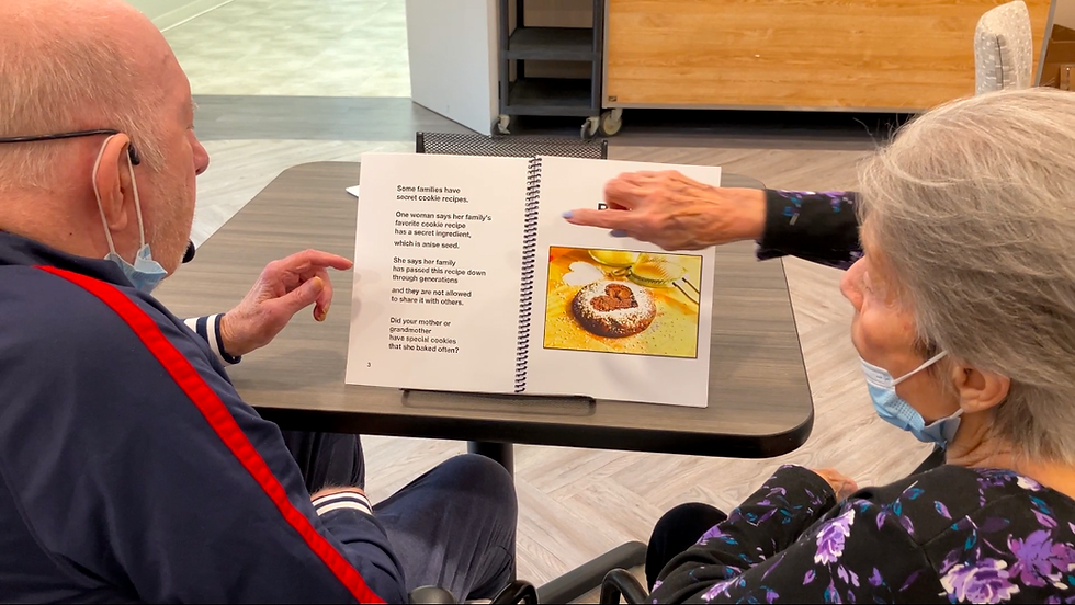 A man and woman read a large print book with a heart-shaped cookie on the page.