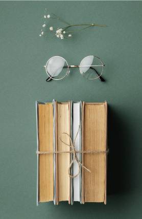Four books bound together with twine sit below a pair of round glasses and a small white budding flower.