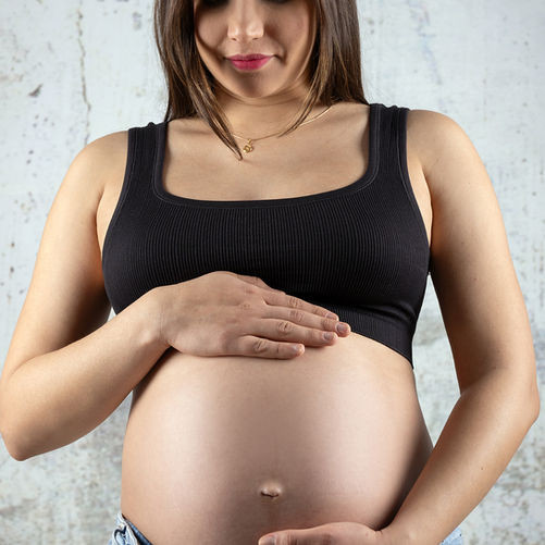 Ruhiges Schwangerschaftsporträt mit natürlicher Pose – moderne Studiofotografie in warmen, neutralen Farben.