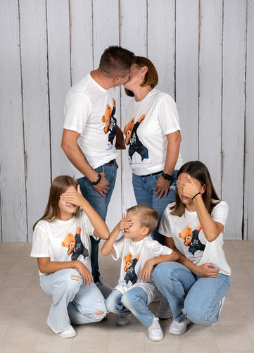 Eltern küssen sich im Studio, drei Kinder sitzen davor und halten sich die Augen zu