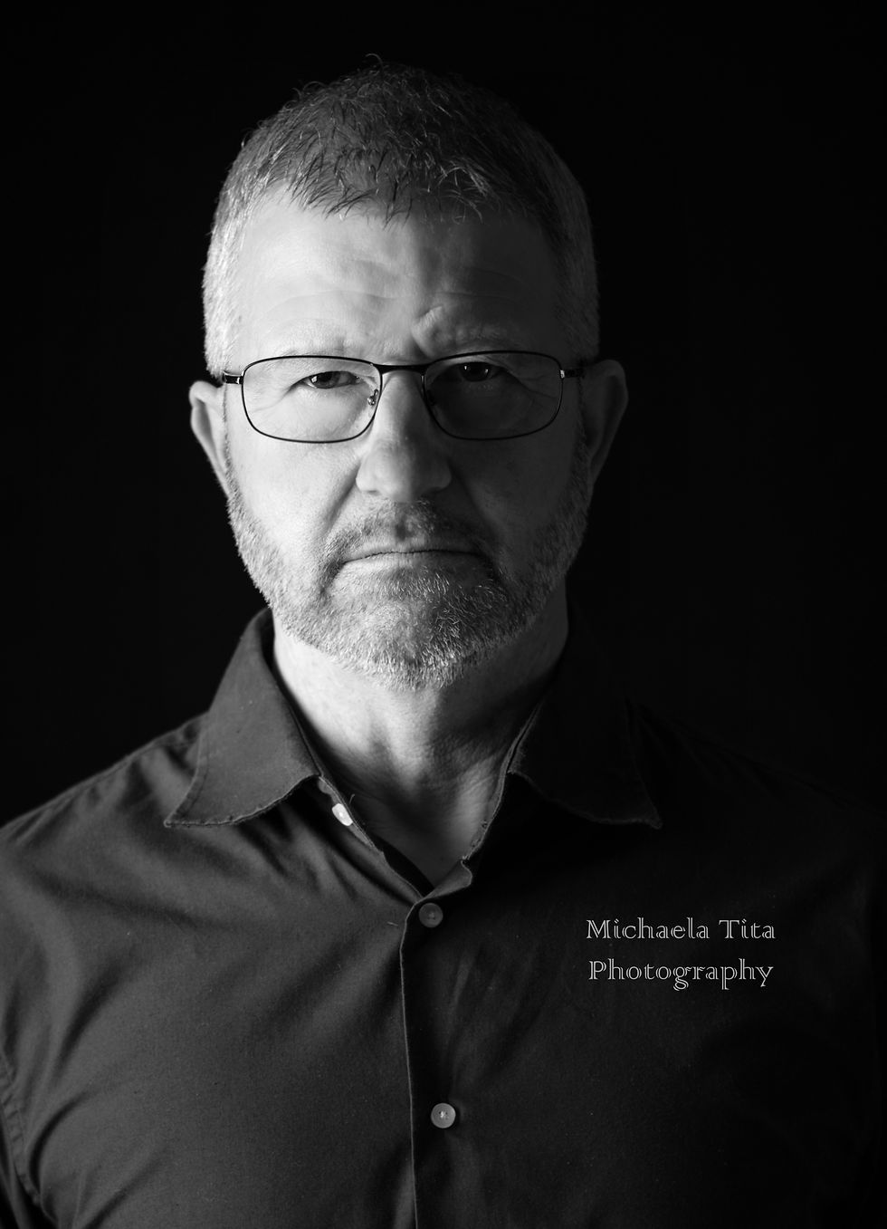 Schwarzweiß-Kopfporträt eines Mannes mit halbseitiger Beleuchtung und ernstem Blick