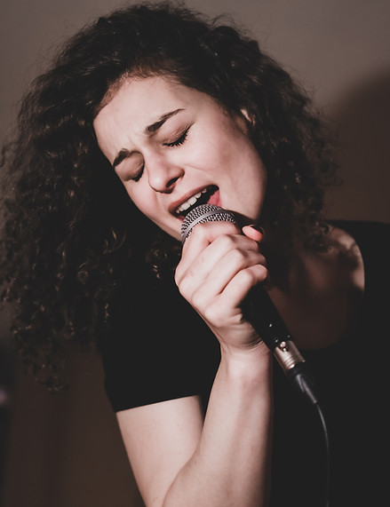 Young woman with curly hair singing, holding microphone.jpg