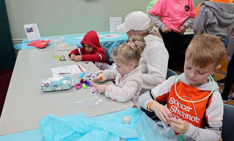 three children play with clay on a table covered in blue plastic