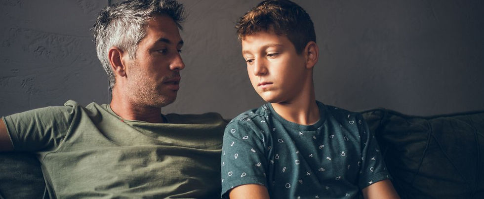 A father looks at his son who is sitting next to him, while his son looks down