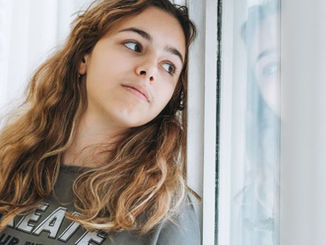 Teen girl leans against a window looking over her shoulder