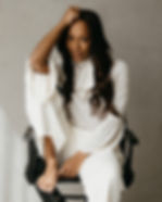 Alyson Joyce, a black woman, with long brown hair, wearing white clothes sitting in a directors chair