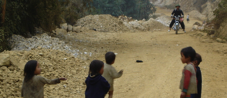Kids playing on a dirt road in Vietnam, greeting passing-by bikers.