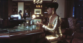 Dark Angels (1998) movie still - Black woman in gold dress lighting a cigarette while sitting at a hotel bar