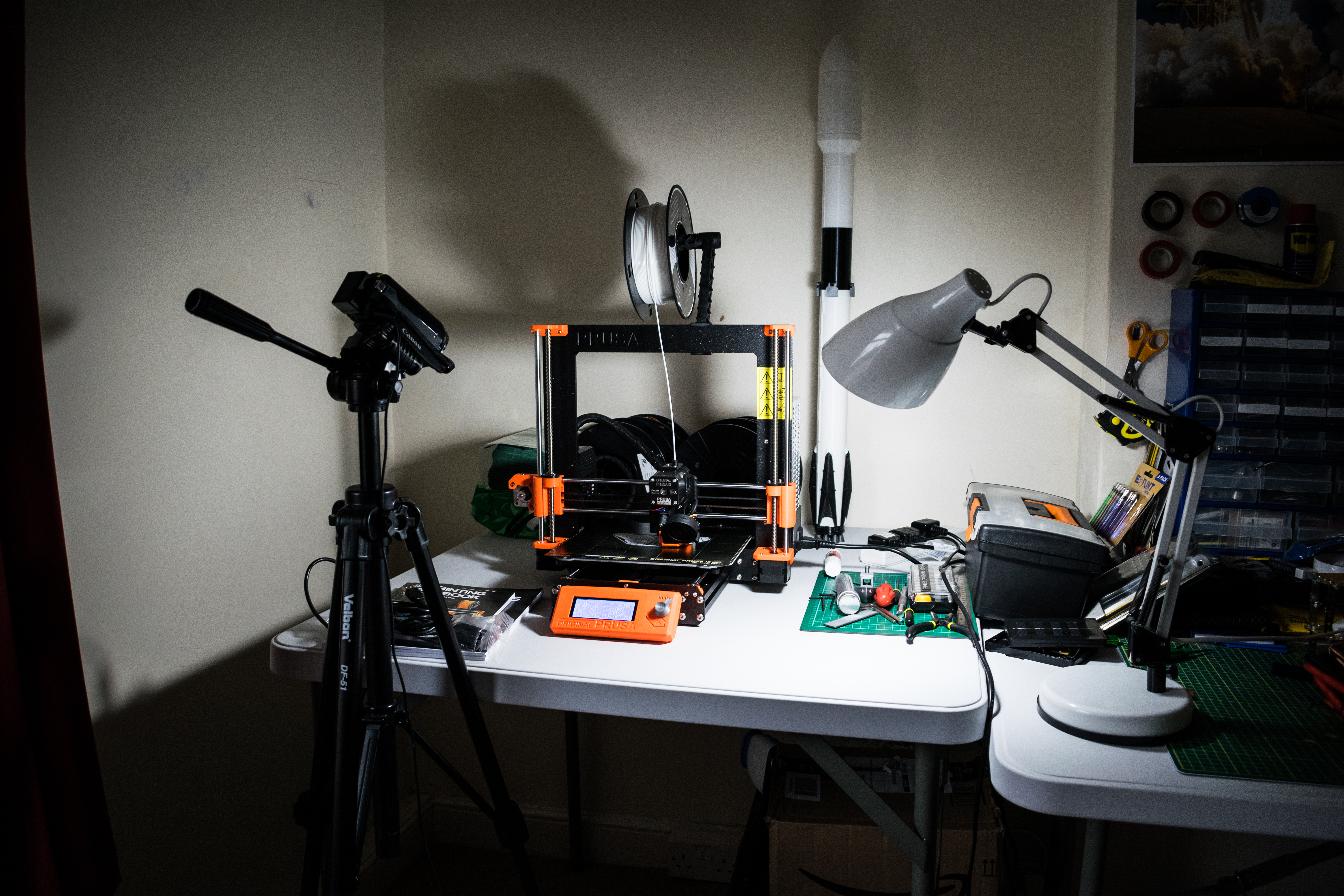 Workshop desk with a 3D printer, a model rocket, and a lamp