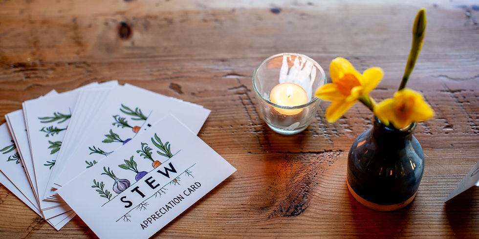 A set of event cards sits on a wooden table next to a candle and flower.