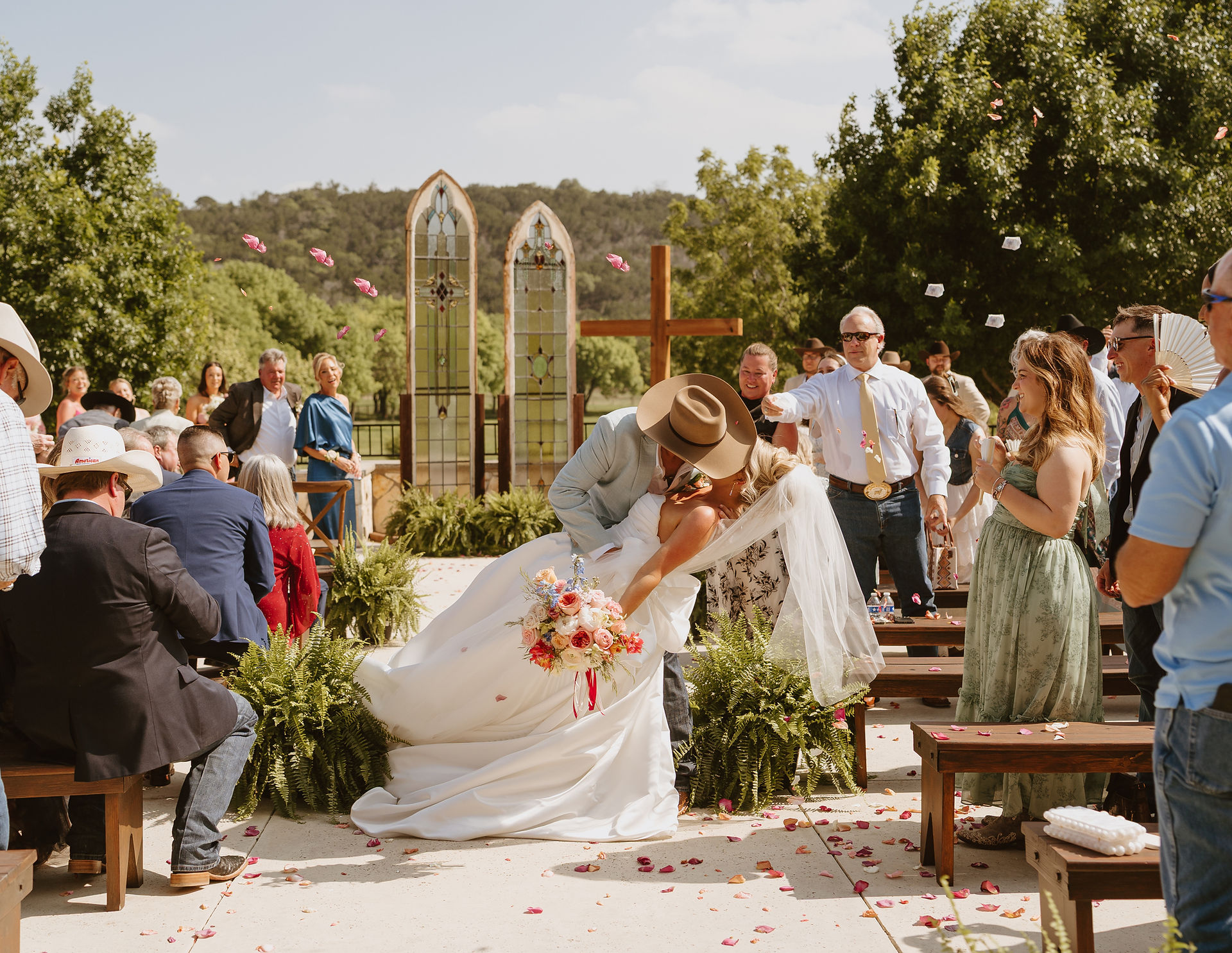Newly married couple kissing in center aisle surrounded by flower petals at Sendera Springs wedding venue