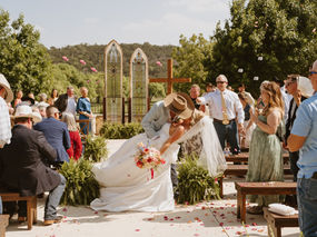 Bride and groom kissing in the ceremony aisle surrounded by flower petals at Sendera Springs wedding venue near Fredericksburg, Texas