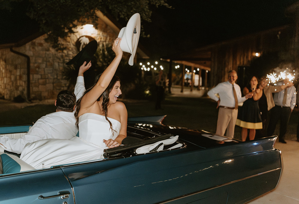 Bride and groom celebrating as they leave their wedding reception in a vintage getaway car.