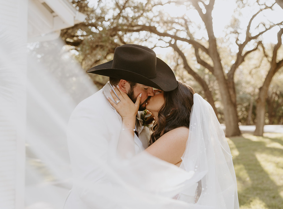 Bride holding the groom's face as they kiss with the veil flowing at The Chandelier of Gruene in Gruene, Texas.