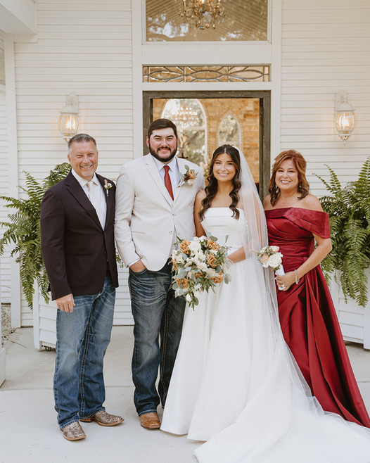 Bride and groom smiling with the bride's parents after the wedding ceremony at The Chandelier of Gruene in Gruene, Texas.