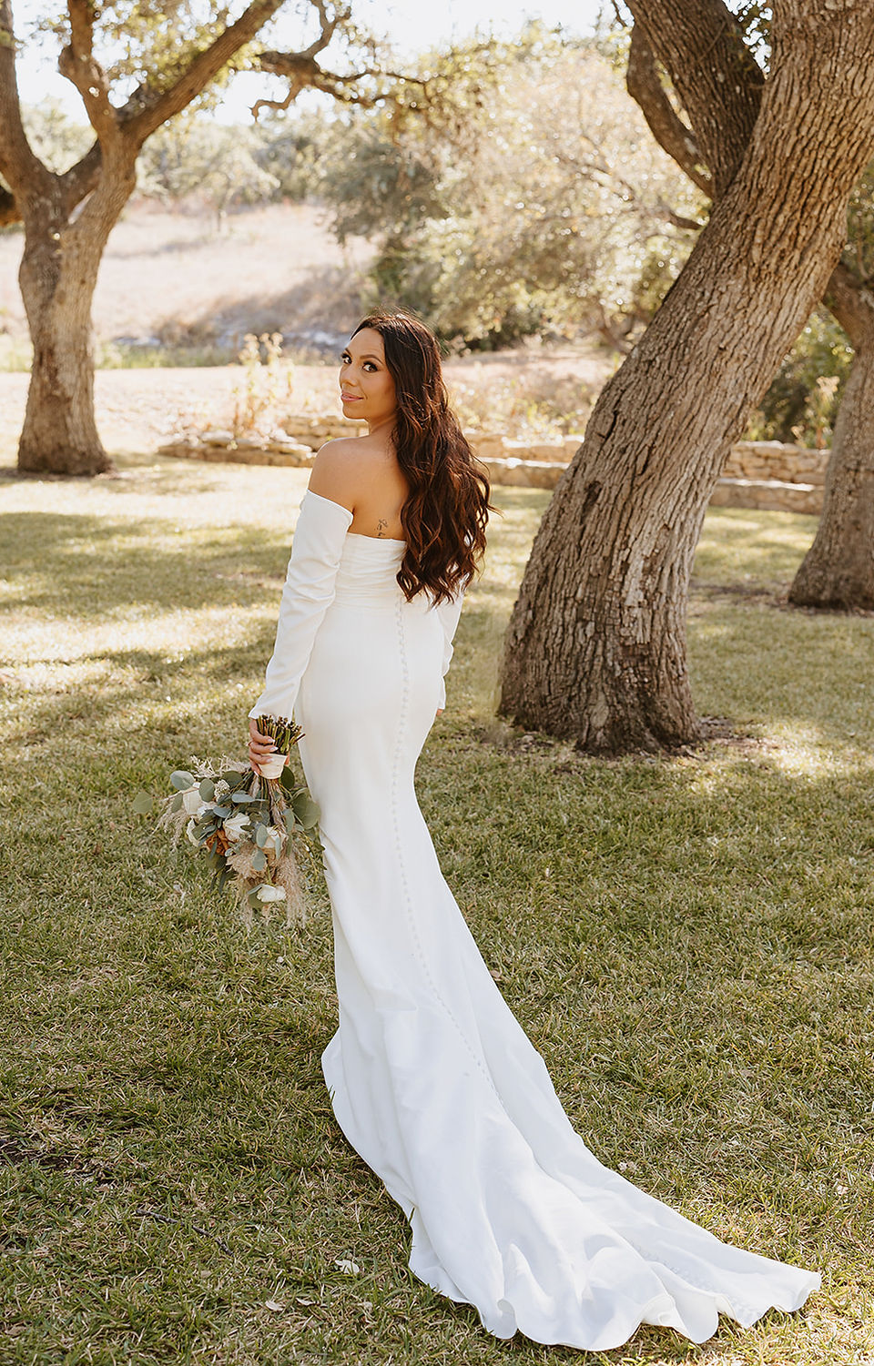 Bride walking across the grounds of The Addison Grove in Dripping Springs, Texas, looking back with a smile during her wedding day, captured by Grace J Photo, a Dripping Springs wedding photographer.
