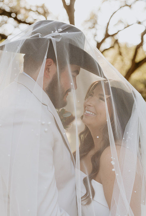 Bride and groom laughing together beneath the wedding veil at The Chandelier of Gruene in Gruene, Texas.