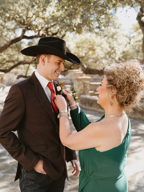Candid moment of the groom putting on his boutonniere at Lost Mission in the Texas Hill Country
