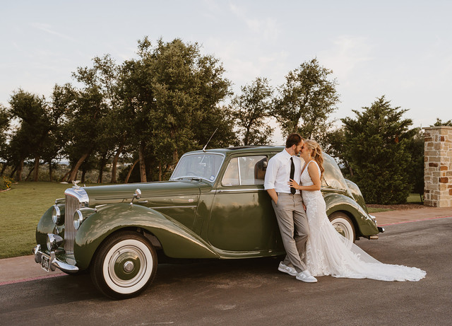 Bride and groom posing with vintage car in editorial style at Canyonwood Ridge Dripping Springs wedding