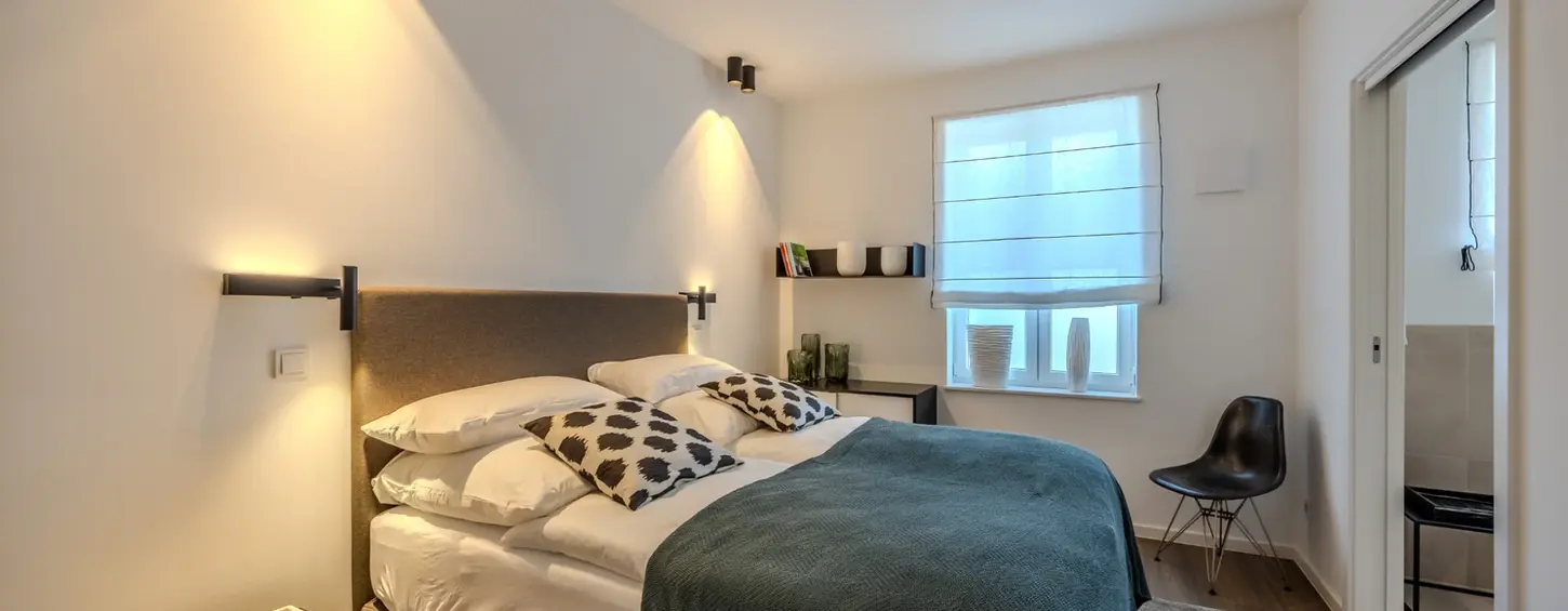 Schlafzimmer mit Wandleseleuchten und Arbeitsbereich in einem vollständig möblierten Apartment L