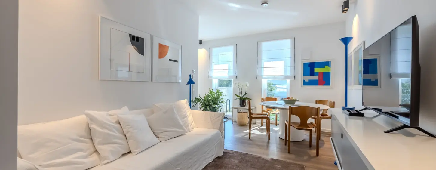 Heller Wohnbereich mit weißem Sofa und Essbereich in einem vollständig möblierten Apartment L